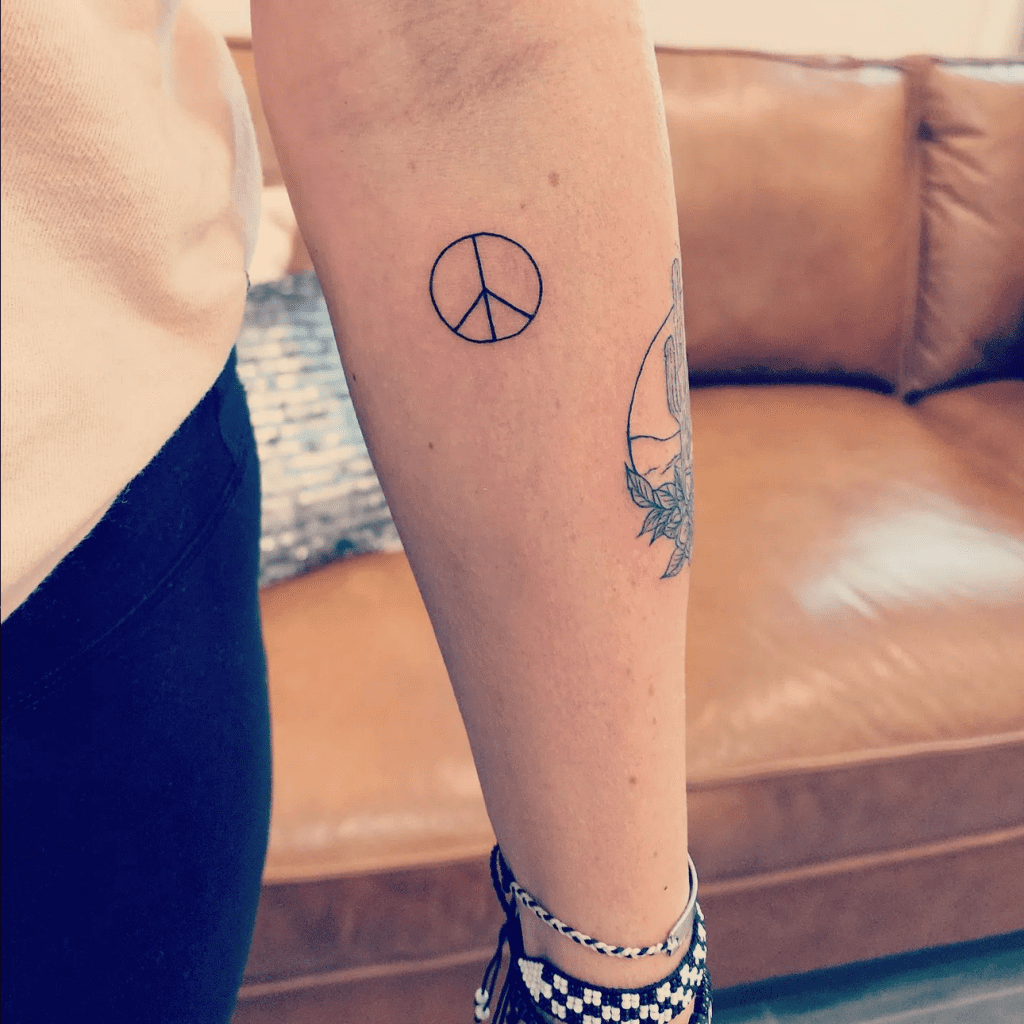 a peace sign fine line tattoo on a forearm